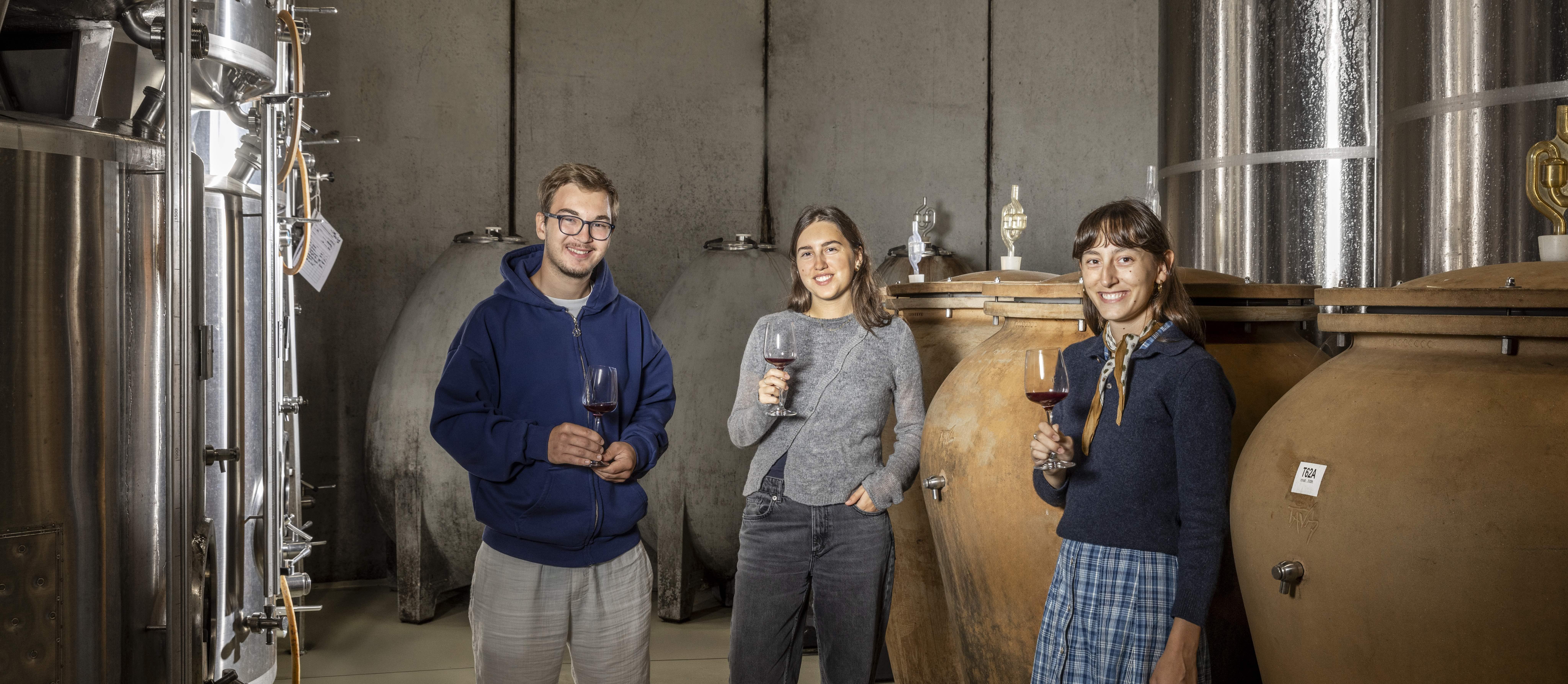 Das Foto zeigt Maximilian, Katharina und Sophie Wieninger bei einer Verkostung im Weinkeller umgeben von Edelstahltanks, Betoneiern und Amphoren, die für die Vinifikation nutzt werden.